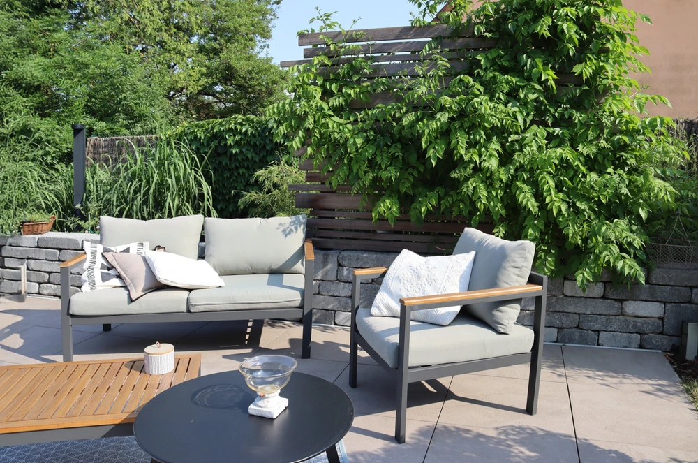 Terrasse extérieure aménagée avec salon de jardin contemporain comprenant canapé et fauteuil à structure aluminium et coussins beiges, table basse ronde noire