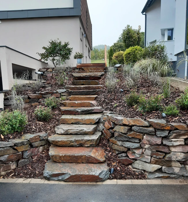 Aménagement paysager extérieur résidentiel avec escalier en pierre naturelle intégré dans un talus végétalisé