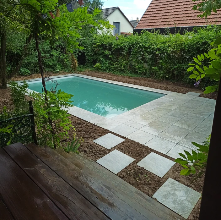 Piscine rectangulaire extérieure avec margelles en pierre naturelle claire, entourée d'un aménagement paysager luxuriant