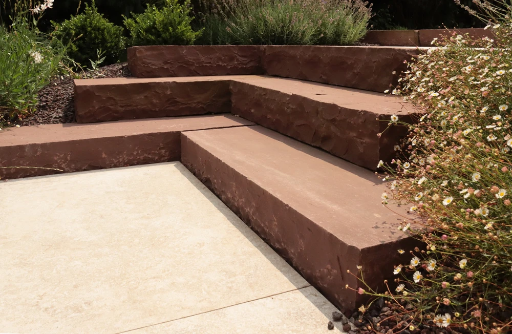 Aménagement paysager extérieur avec escalier en pierre reconstituée rouge-brun intégrant banquettes d'angle
