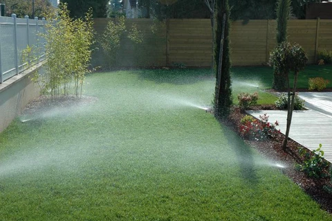 Jardin résidentiel avec système d'arrosage automatique en fonctionnement, jets d'eau pulvérisés sur pelouse verte