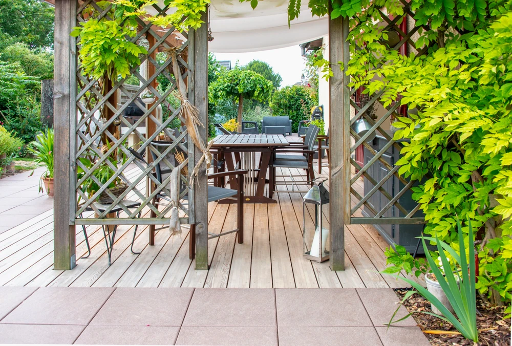 Terrasse extérieure aménagée avec pergola en bois et treillis, mobilier de jardin comprenant table et chaises en teck, végétation luxuriante avec plantes grimpantes
