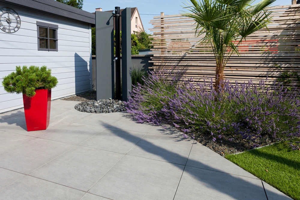 Terrasse extérieure avec piscine rectangulaire aux eaux turquoise, entourée de dalles en béton gris clair disposées en motif régulier