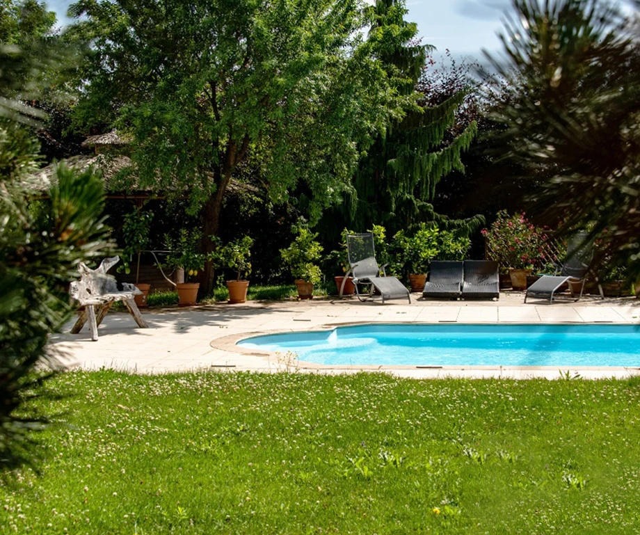 Jardin contemporain avec piscine rectangulaire à débordement, escalier en béton teinté rouge-brun menant à la terrasse dallée beige